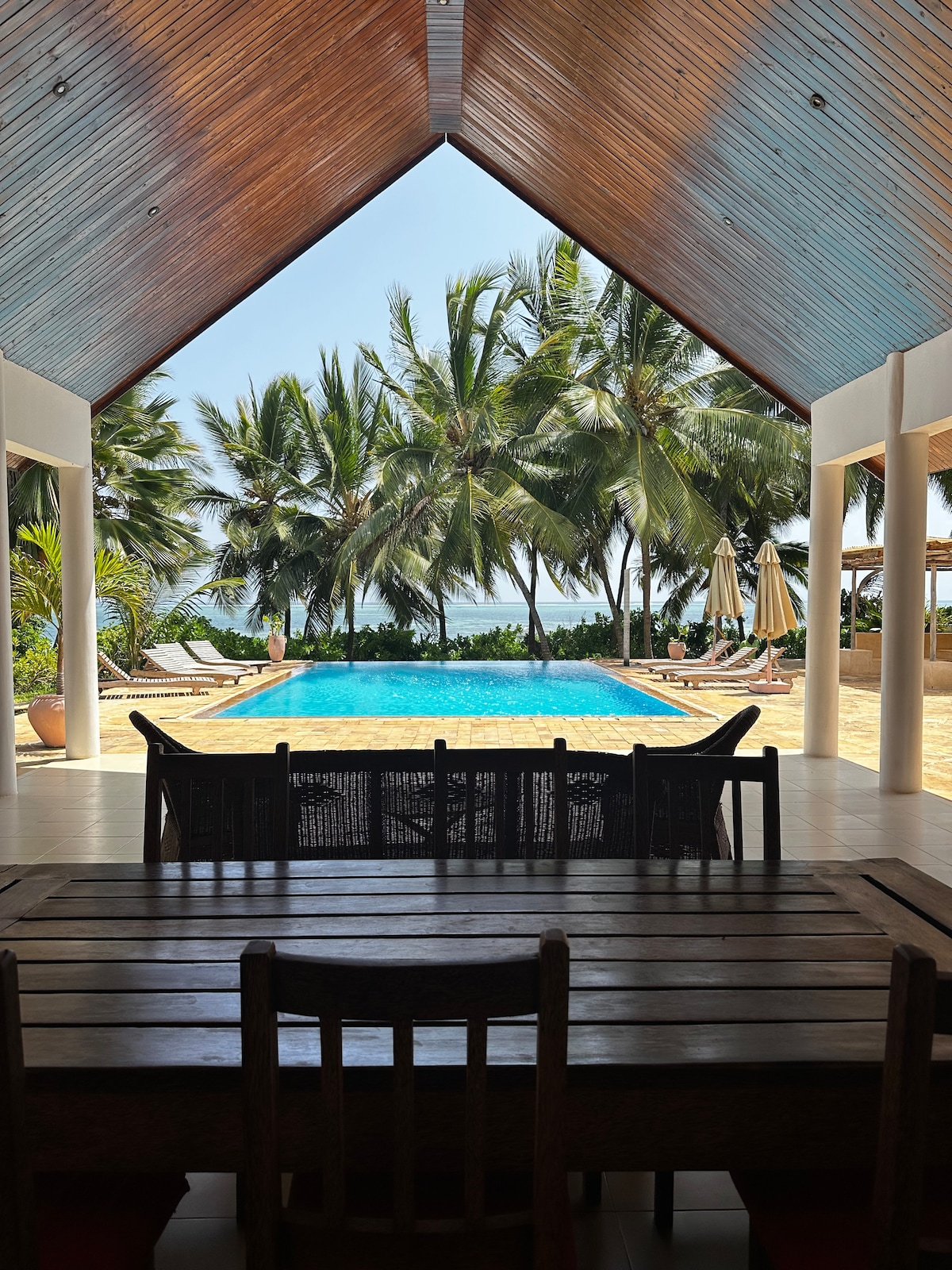 Dining table framing the gable opening to pool, palms and ocean
